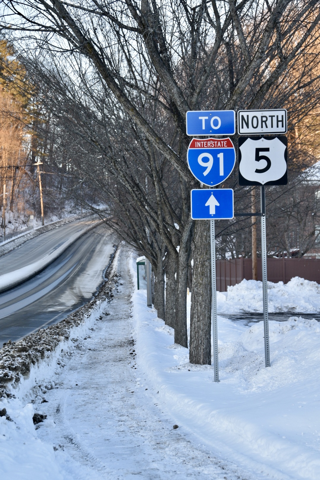 Highway signs for Interstate 91 North and US Route 5 amid snow and bare trees